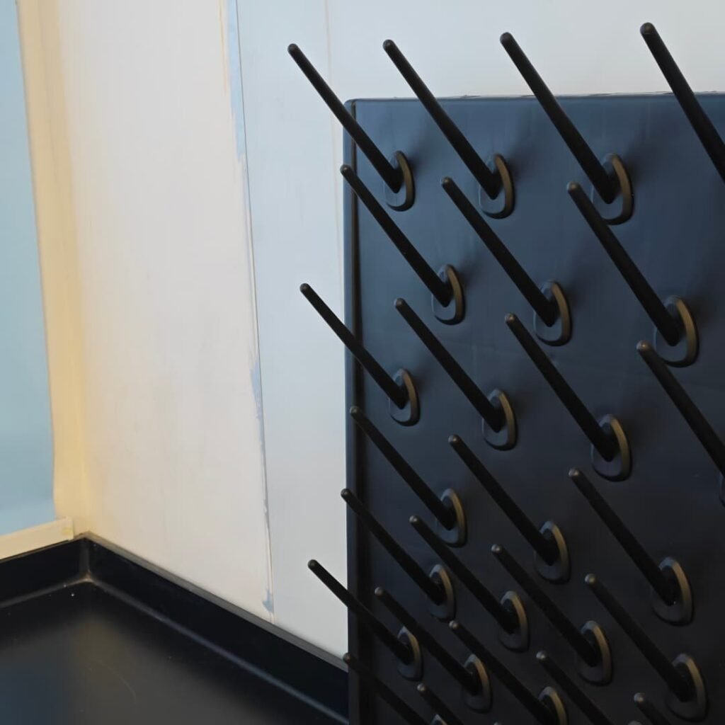 Wall-mounted glassware drying rack with angled black pegs and drain tray